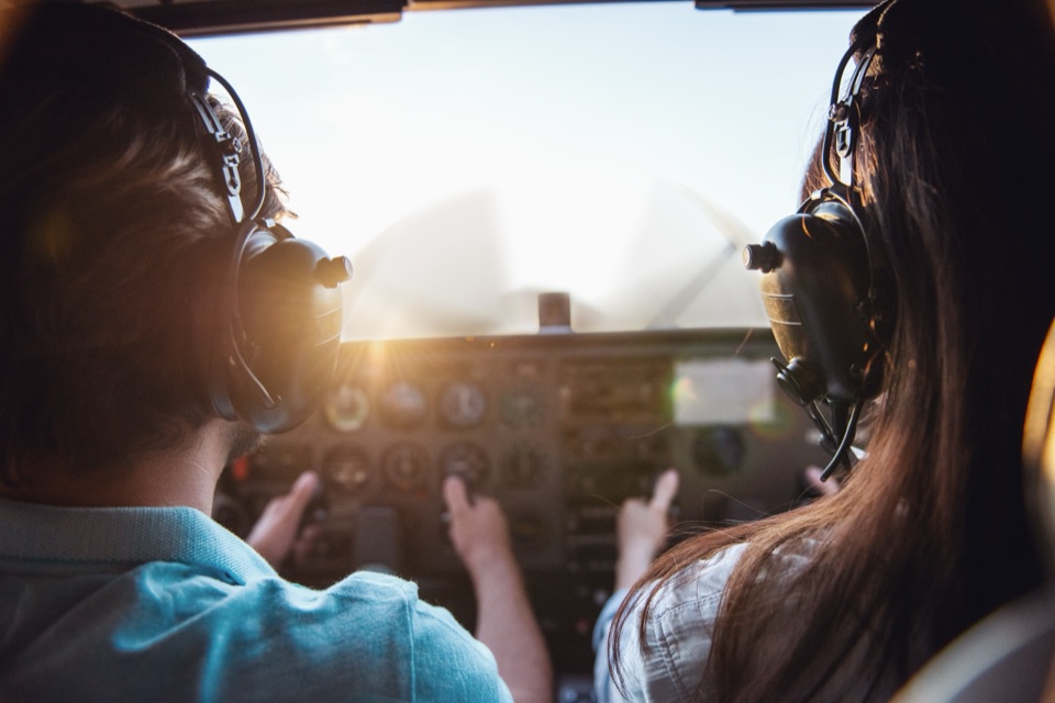 An instructor and student in the cockpit of a training aircraft, the instructor pointing out a gauge
