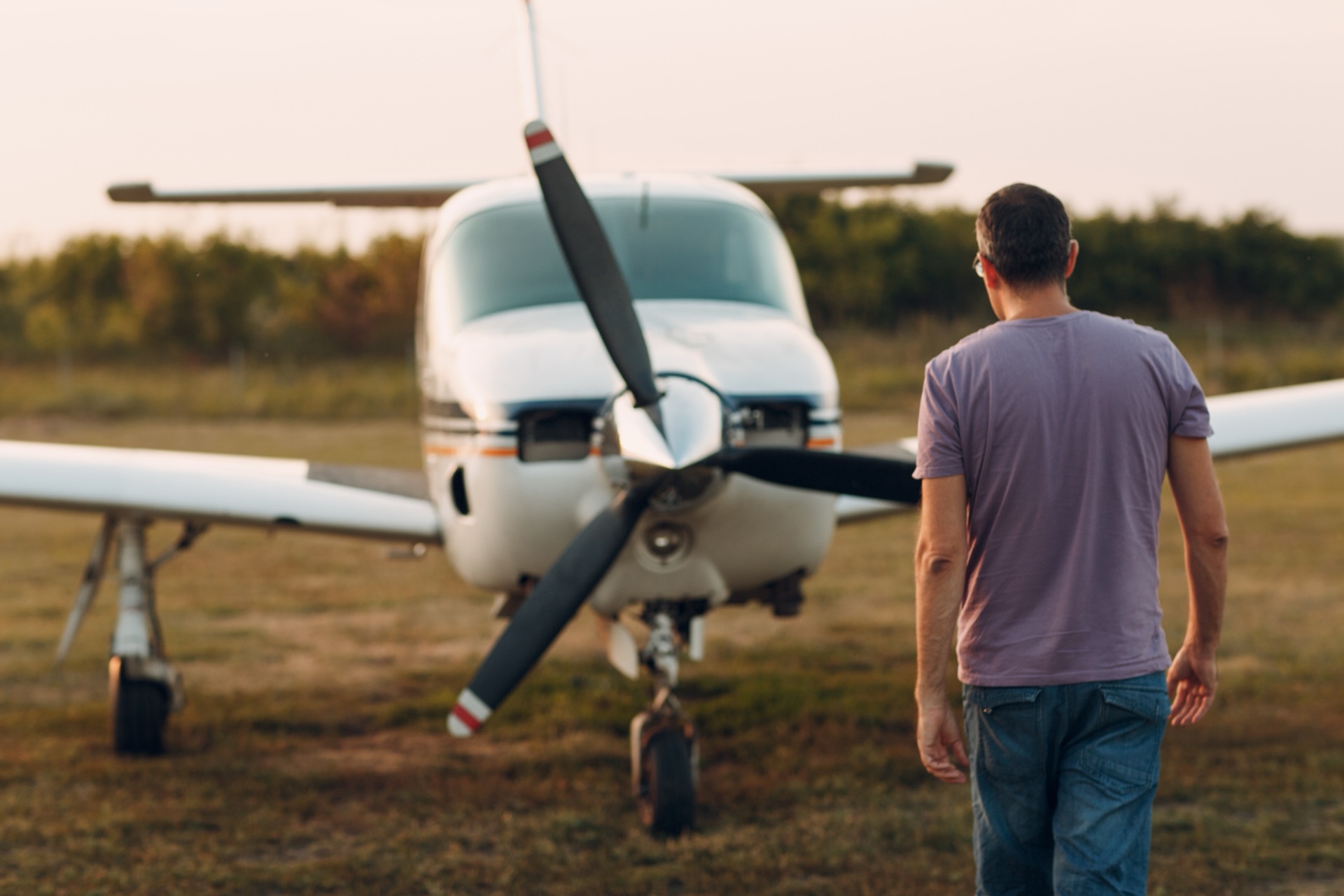 An aircraft owner walking out to a parked piston single on a grass strip at golden hour